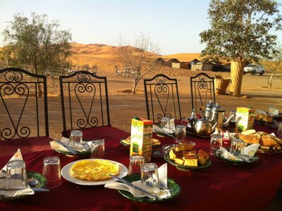 Food and drink placed on table with trees and sand dunes in background, Morocco