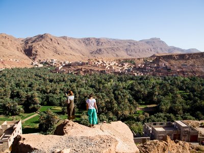 Two people taking in view of Moroccan village in the distance whilst standing atop a cliff, Morocco
